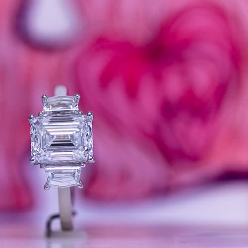 Three stone diamond ring with emerald cut center and heart background.