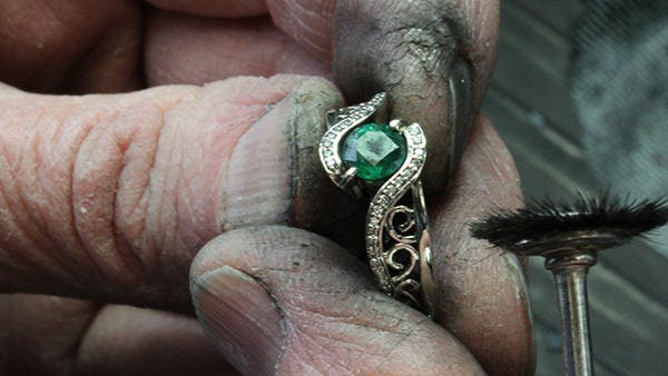 Marsha polishing a yellow gold ring set with a round green emerald.