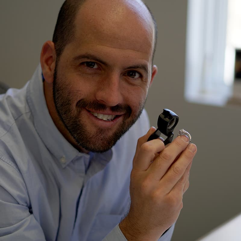 Joseph Dolginow in the jewelry office evaluating a diamond ring.