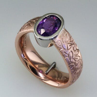 Shoulder view of oval purple sapphire in rose gold ring