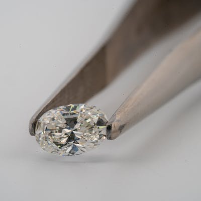 oval diamond 3/4 carat GIA held in tweezers