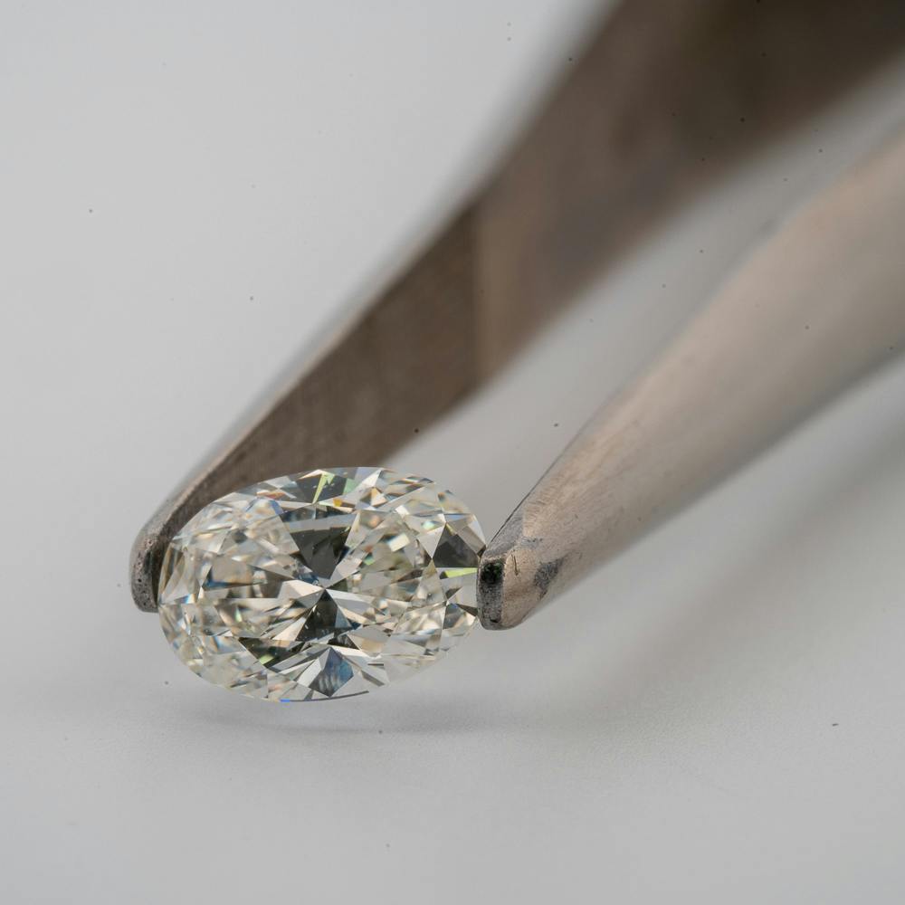 oval diamond 3/4 carat GIA held in tweezers